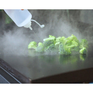 A Blackstone plastic basting bottle squirting water on broccoli on a griddle